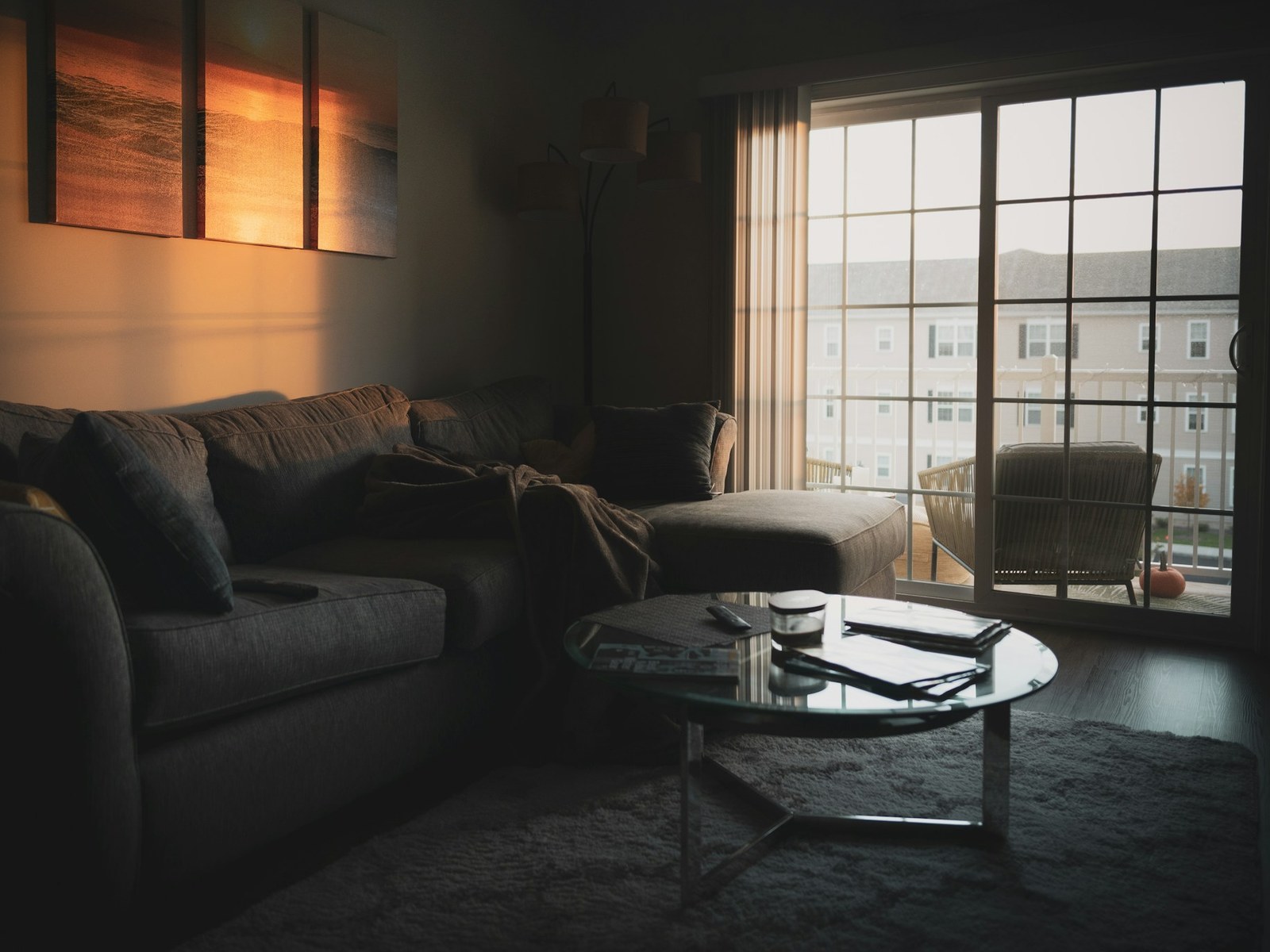 Dim living room with a gray area rug, scattered magazines and an untidy throw before editing